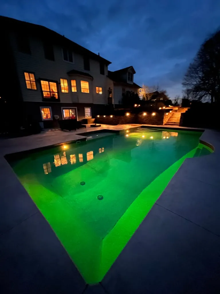 In ground pool glowing at night beside the house
